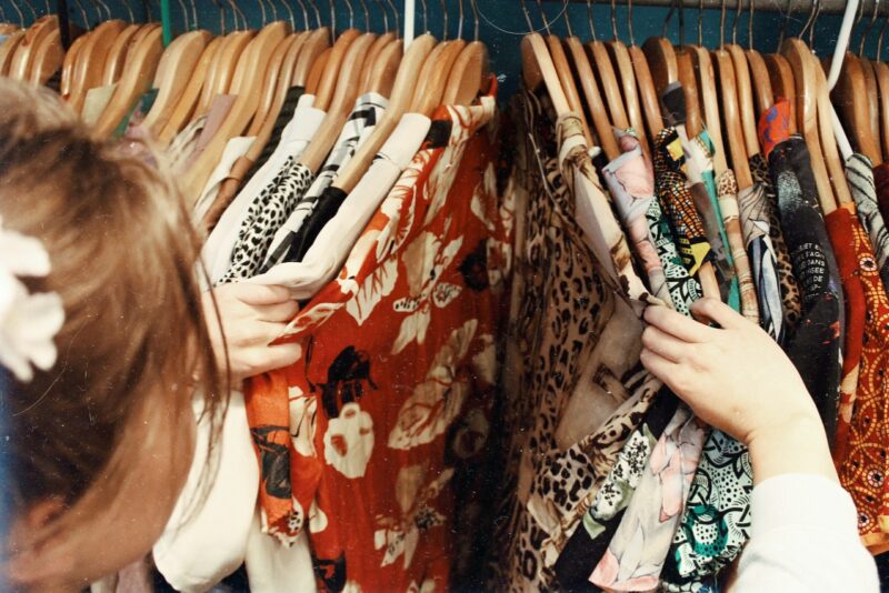 Person hält verschiedene Vintage-Kleidung in einem hölzernen Kleiderbügel